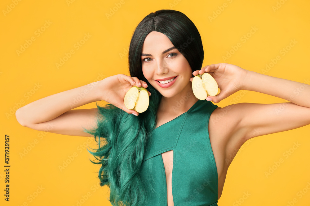 Beautiful young woman in wig and with apple on color background