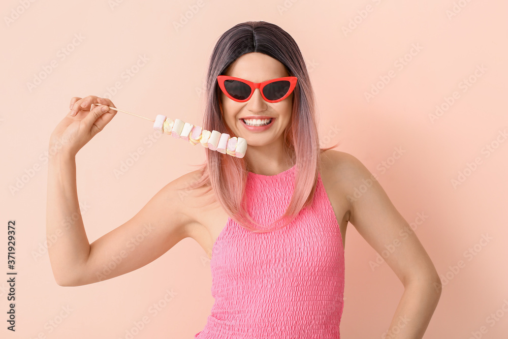 Beautiful young woman in wig and with marshmallow on color background