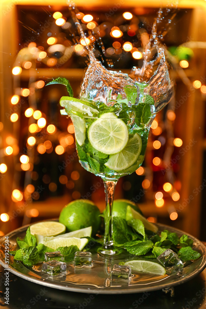 Glass of fresh mojito with splash on table against blurred lights