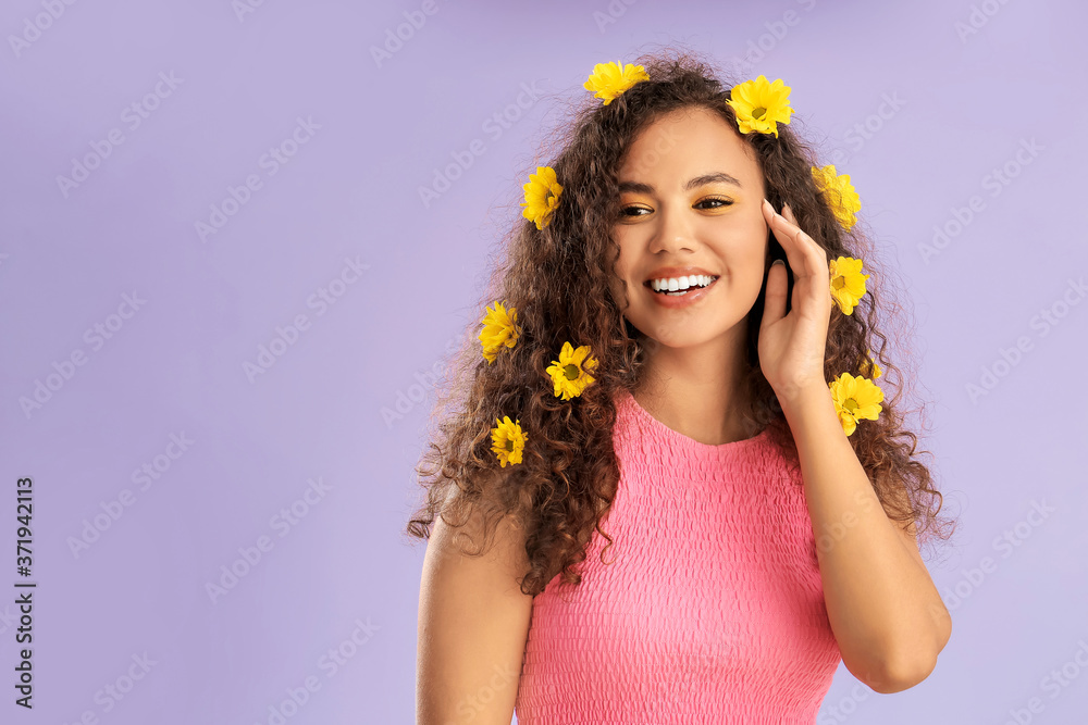 Young African-American woman with beautiful eyeshadows and flowers in her hair on color background