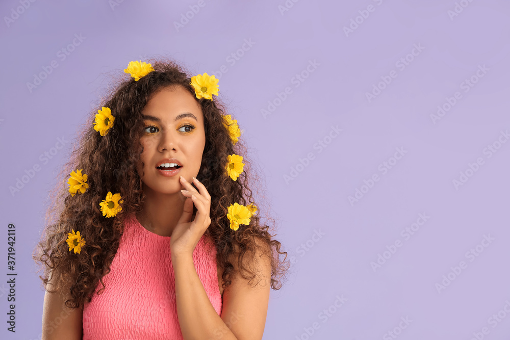 Young African-American woman with beautiful eyeshadows and flowers in her hair on color background