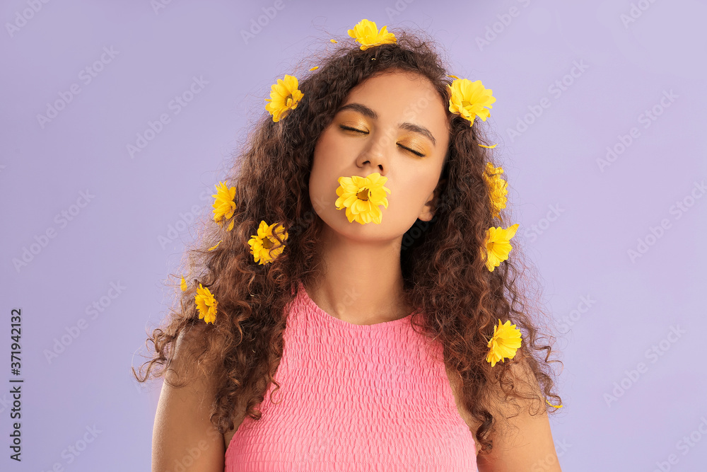 Young African-American woman with beautiful eyeshadows and flowers in her hair on color background