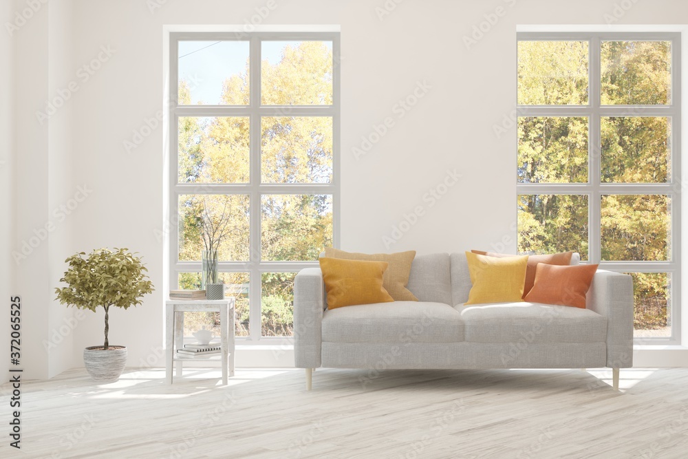 Stylish room in white color with sofa and autumn landscape in window. Scandinavian interior design. 