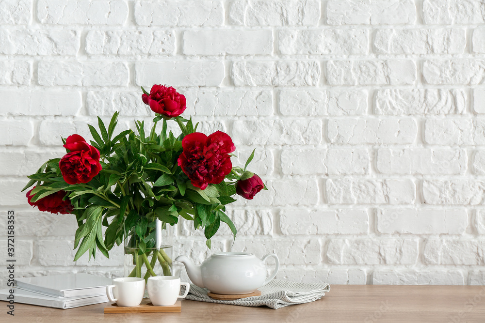 Teapot with cups and bouquet of flowers on kitchen counter