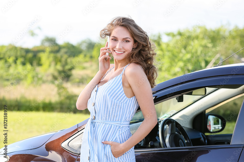 Young woman talking by mobile phone near new car outdoors