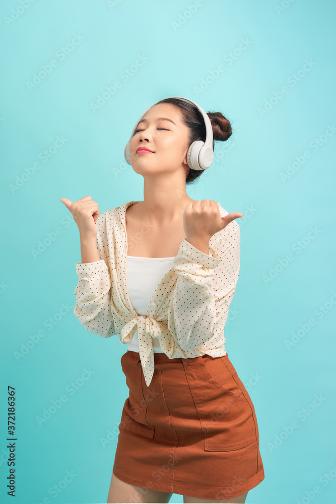 Portrait of a smiling satisfied girl listening to music with headphones while standing with eyes clo