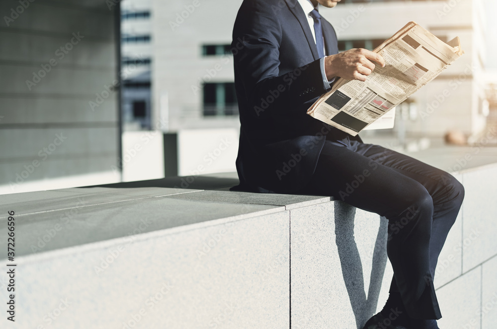 Businessman sitting outside an office building reading a financi