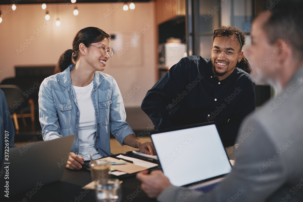 Smiling young businesspeople talking together around an office t