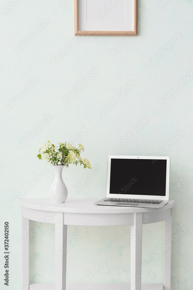 Table with laptop near white wall in room