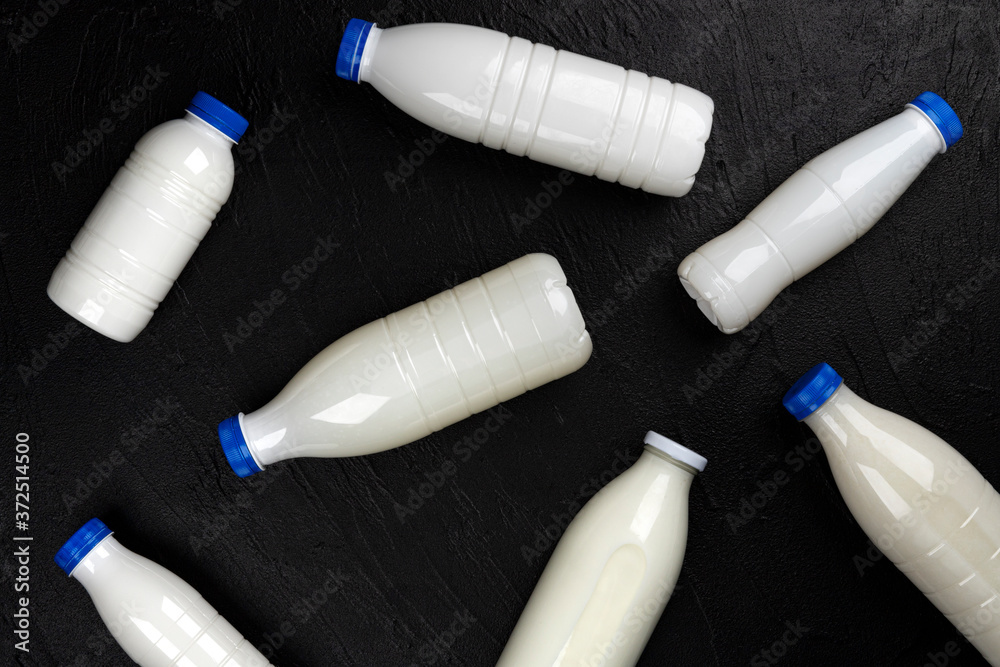 Dairy products packaging, bottles and glasses with milk on black background, top view