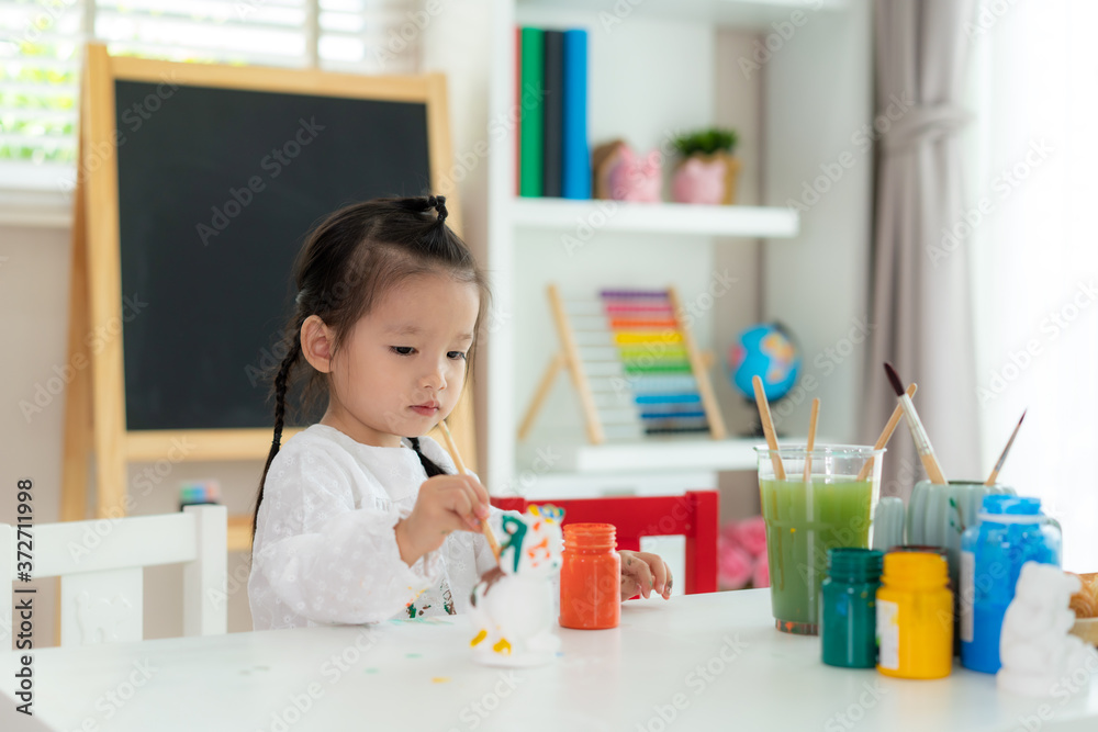 亚洲幼儿园女孩在客厅a用丙烯酸水彩画石膏娃娃