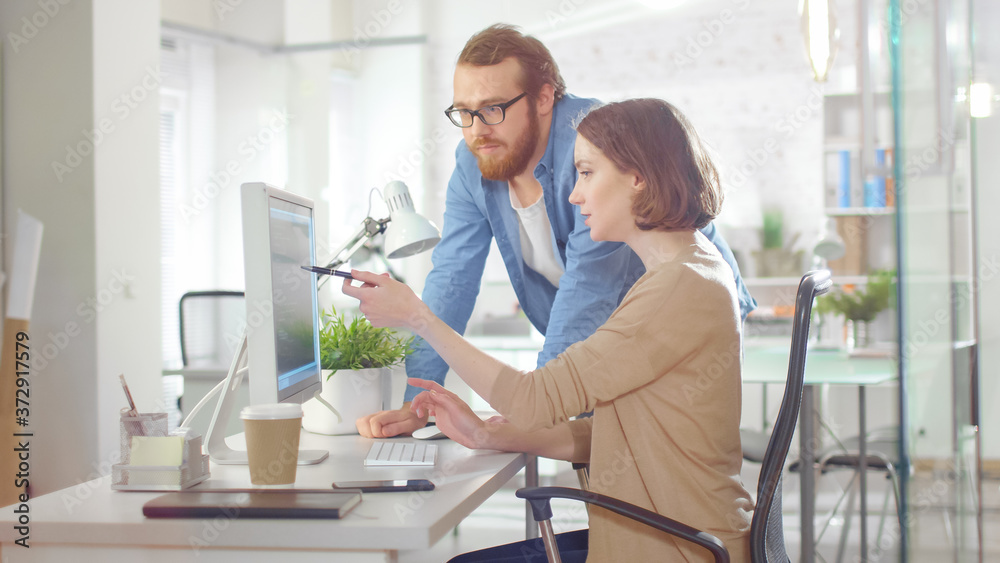 Young Male Manager and Beautiful Woman Discuss Working Issues at Workplace. She is Using Computer an