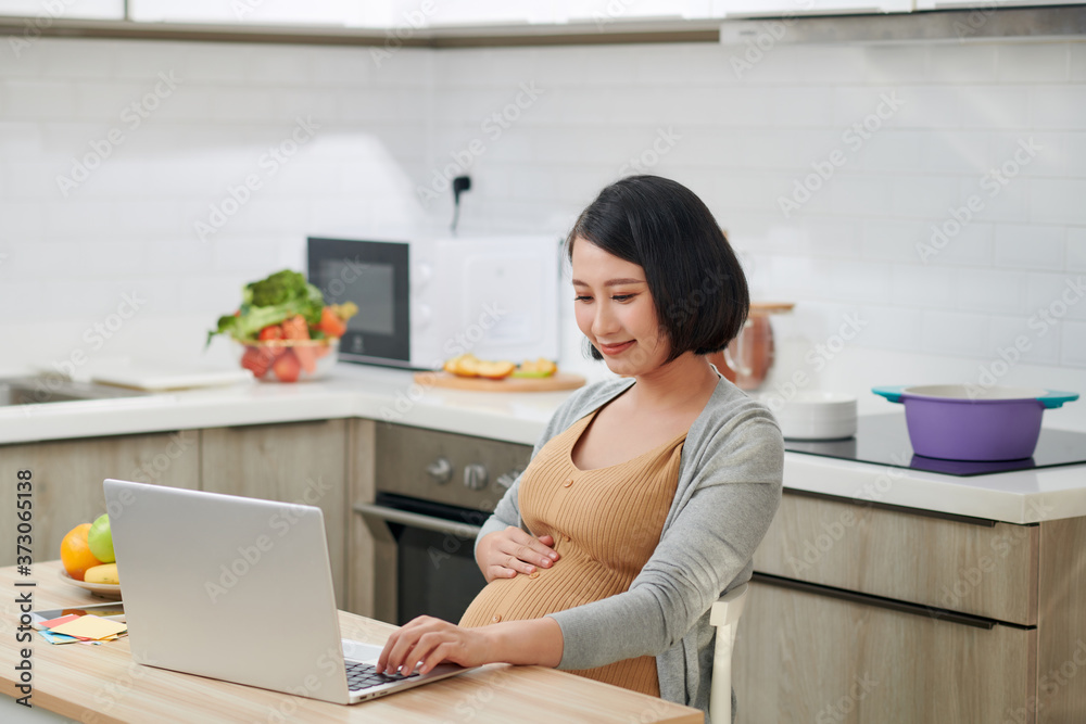 侧视图迷人而进步的年轻妈妈坐在桌子后面的椅子上，明亮