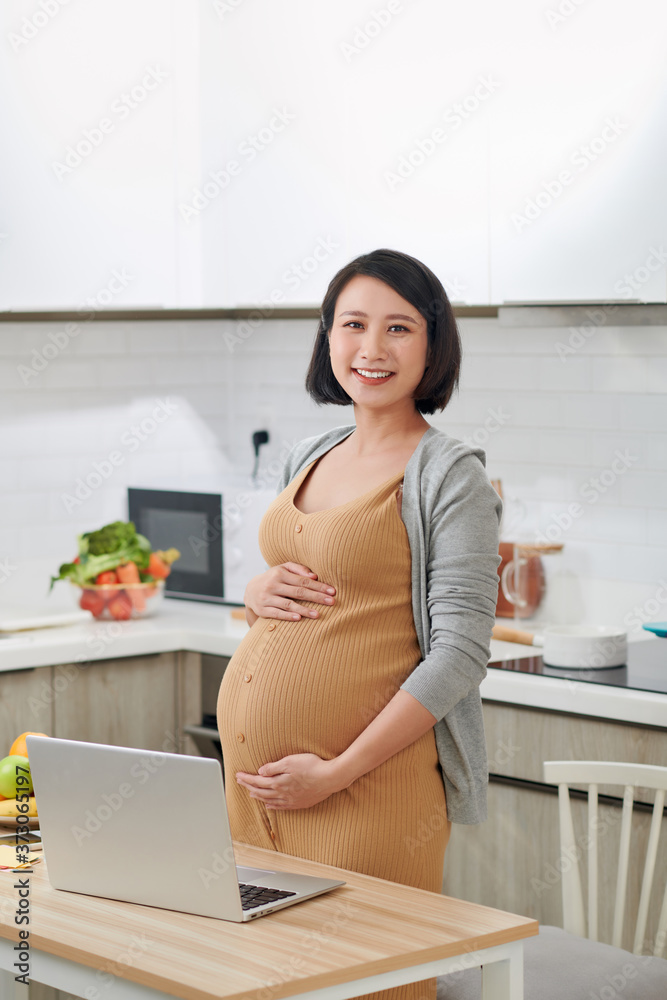 漂亮的年轻女人在厨房里用笔记本电脑