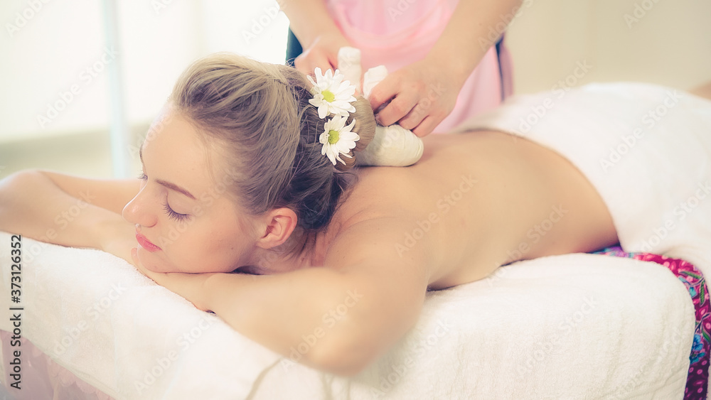 Massage therapist holds a herbal compress to do treatment to woman lying on spa bed in a luxury spa 