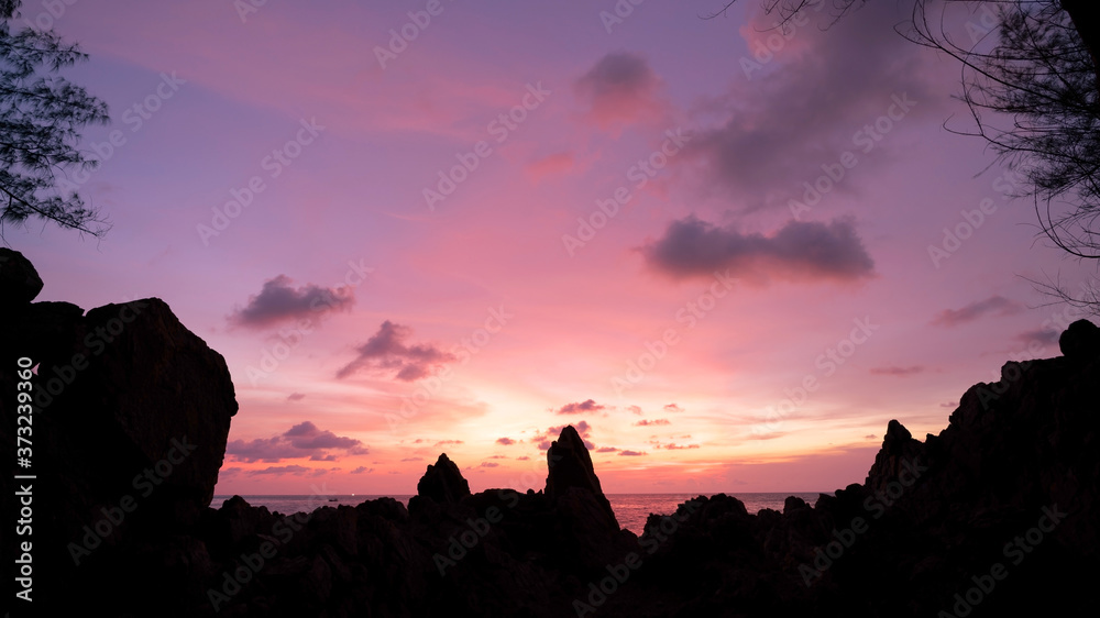 戏剧性的天空海景的长曝光图像，前景是日落或日出的岩石