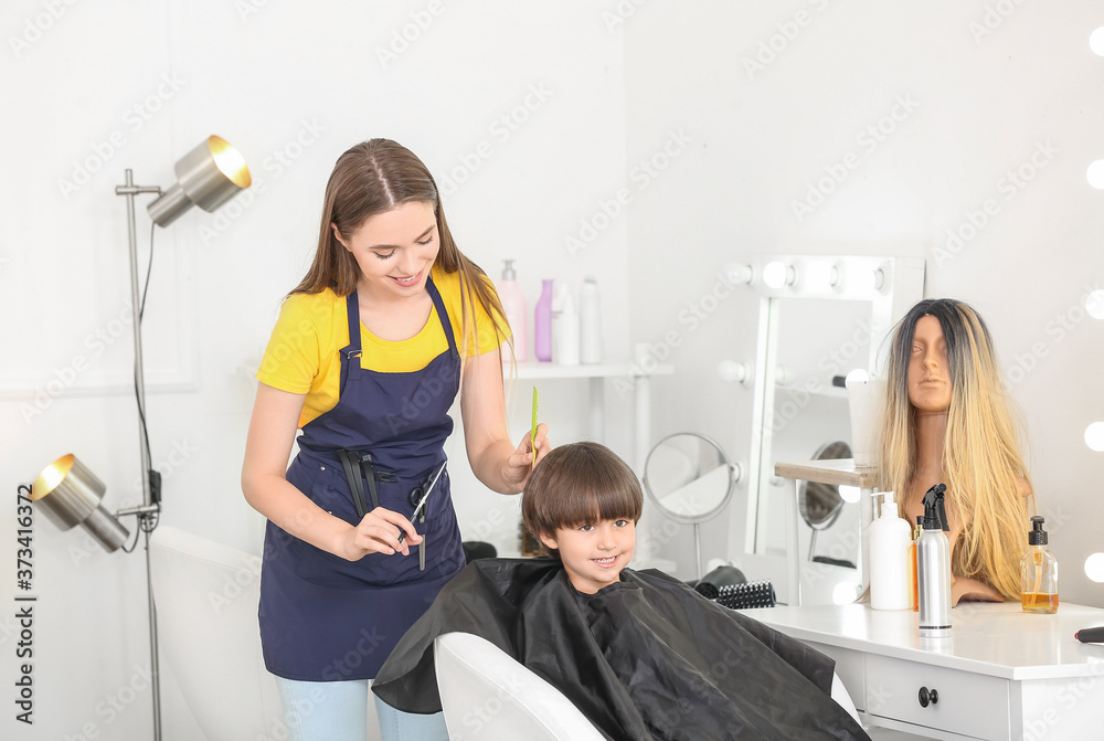 Female hairdresser working with little boy in salon