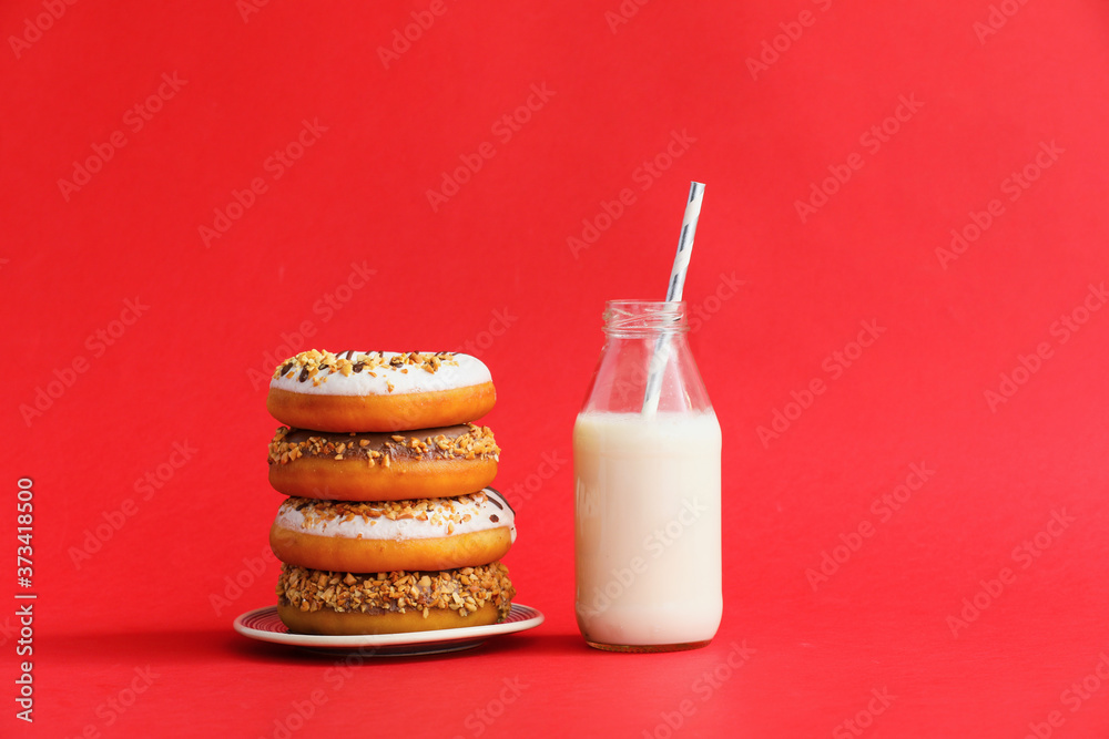 Milk and tasty donuts on color background