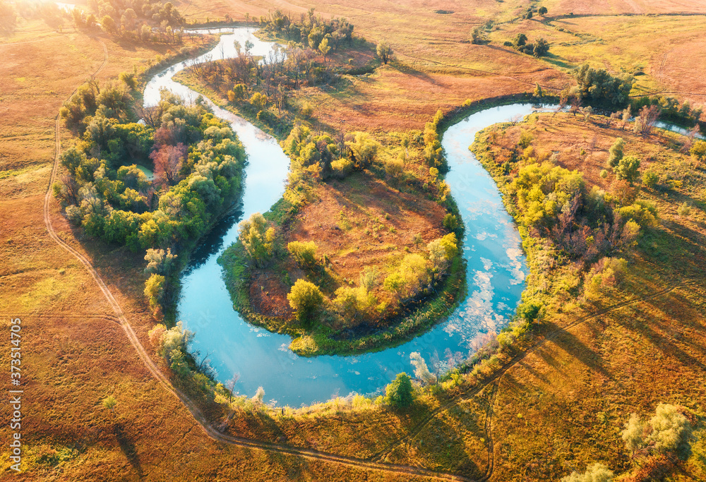 Aerial view of beautiful curving river at sunrise in autumn. View from air. Turns of river, meadows,