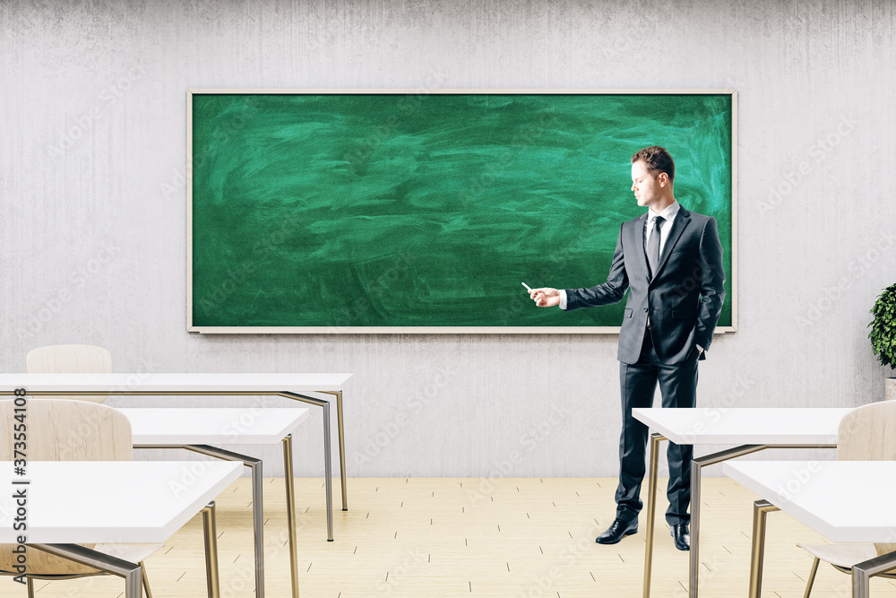 Businessman standing in modern classroom with empty chalkboard