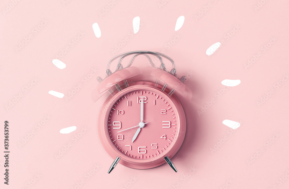 Classic pink alarm clock ringing at seven oclock against pastel pink background