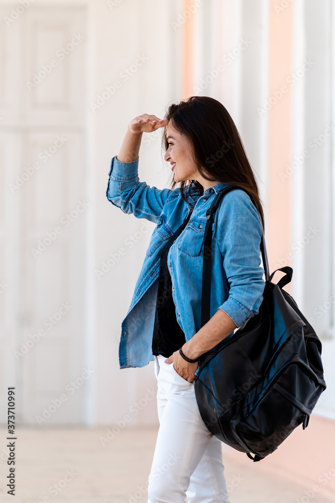 背着背包的漂亮女人。穿着蓝色衬衫和白色牛仔裤的年轻女人的照片。看着si