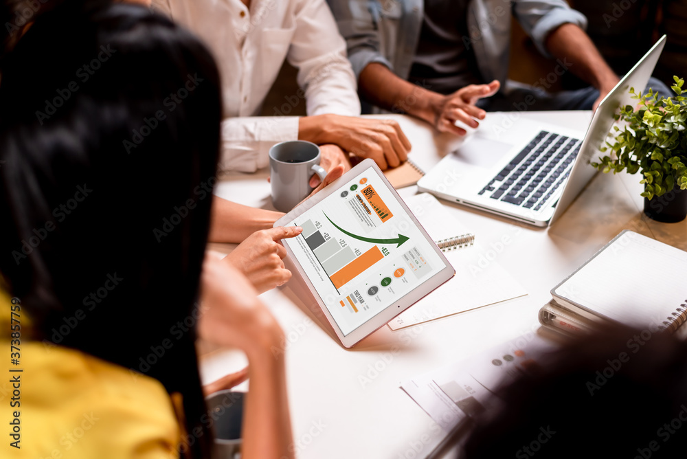 People in meeting room brainstorming while working on performance chart on tablet and computer at ni