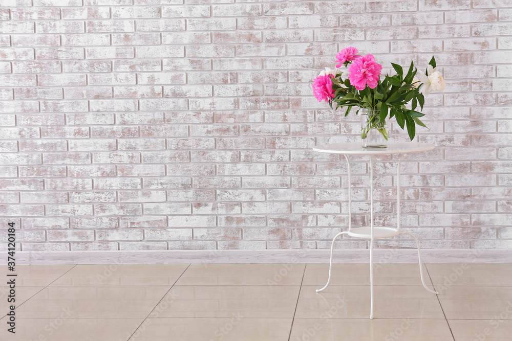 Vase with beautiful flowers on table near brick wall