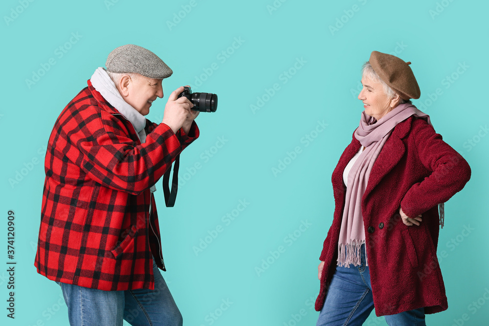 Happy senior couple with photo camera on color background