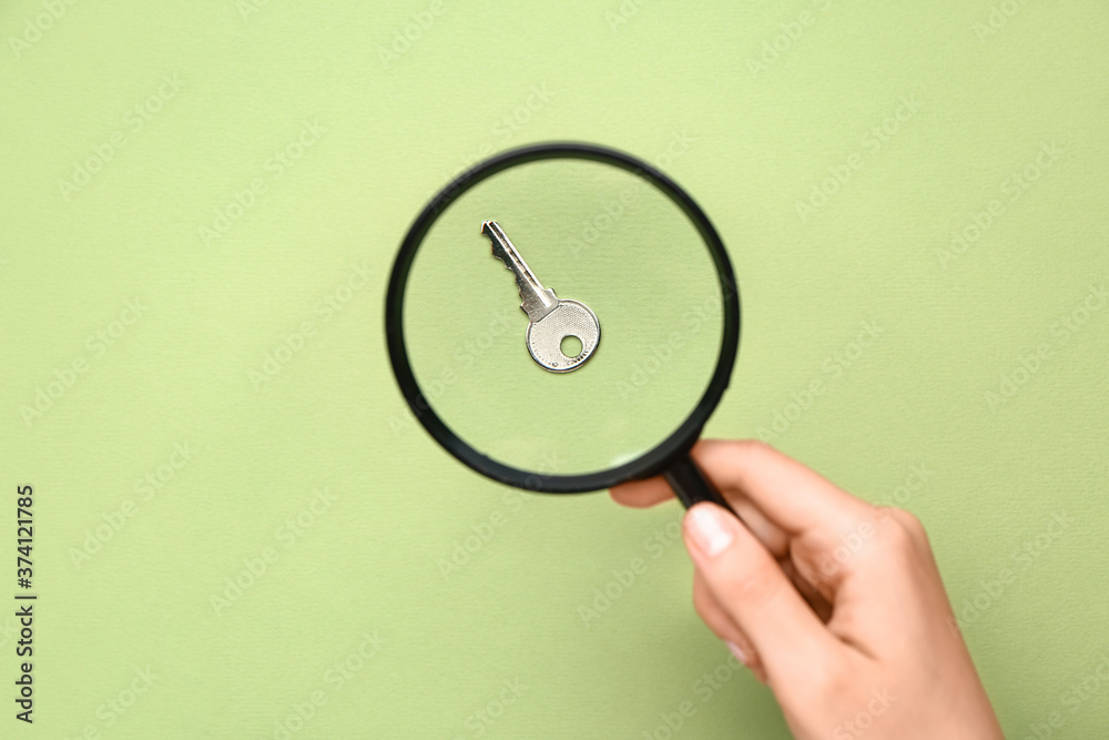 Female hand with magnifier and key on color background