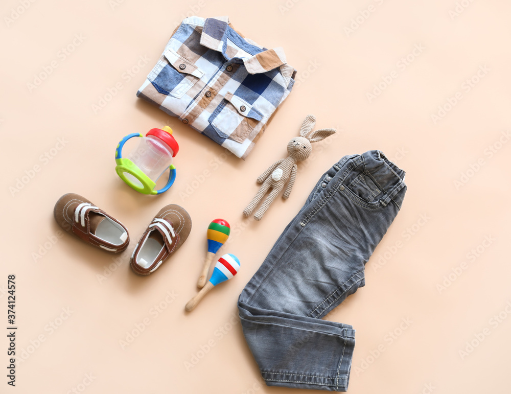 Baby clothes with bottle and toys on color background