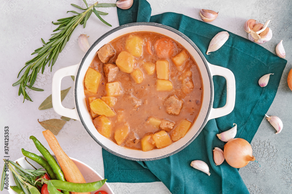 Pot with tasty beef stew on light background