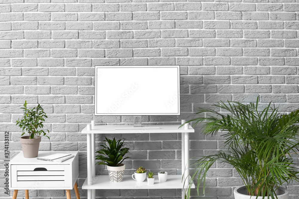 Modern TV set on stand near brick wall in room