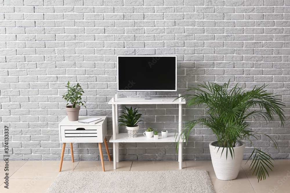 Modern TV set on stand near brick wall in room