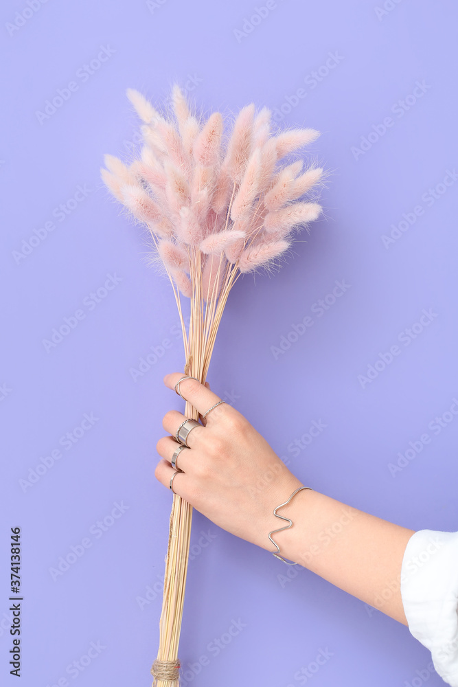 Hand of beautiful young woman with stylish jewelry and floral decor on color background