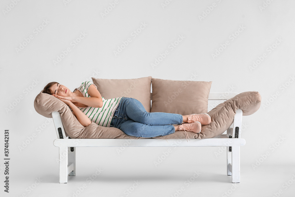 Young woman sleeping on modern sofa against light background