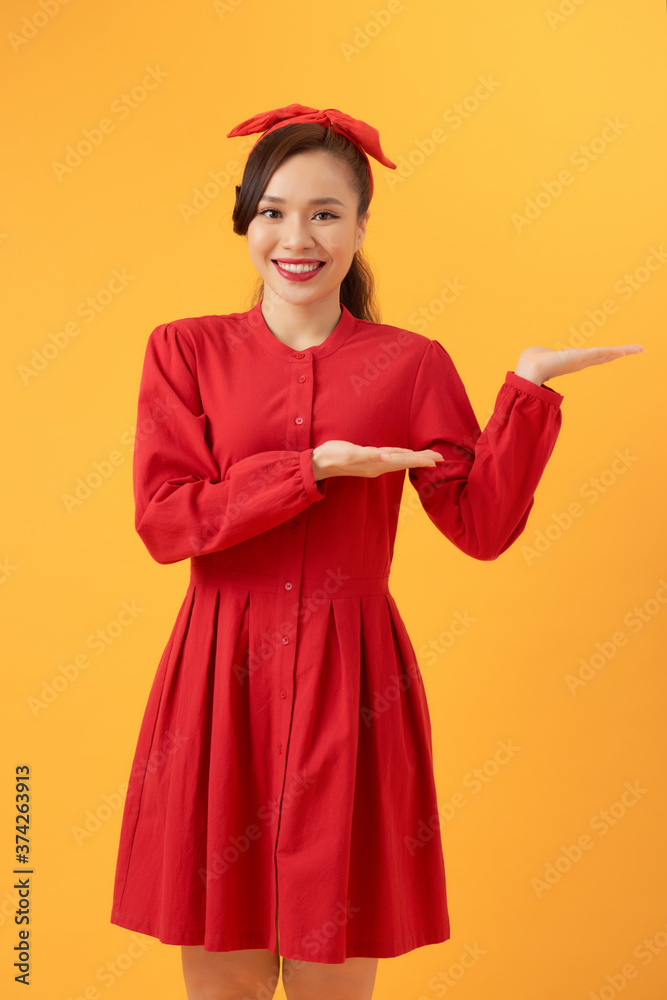 Young Asian Woman in red dress pointing to copy space, isolated on orange background