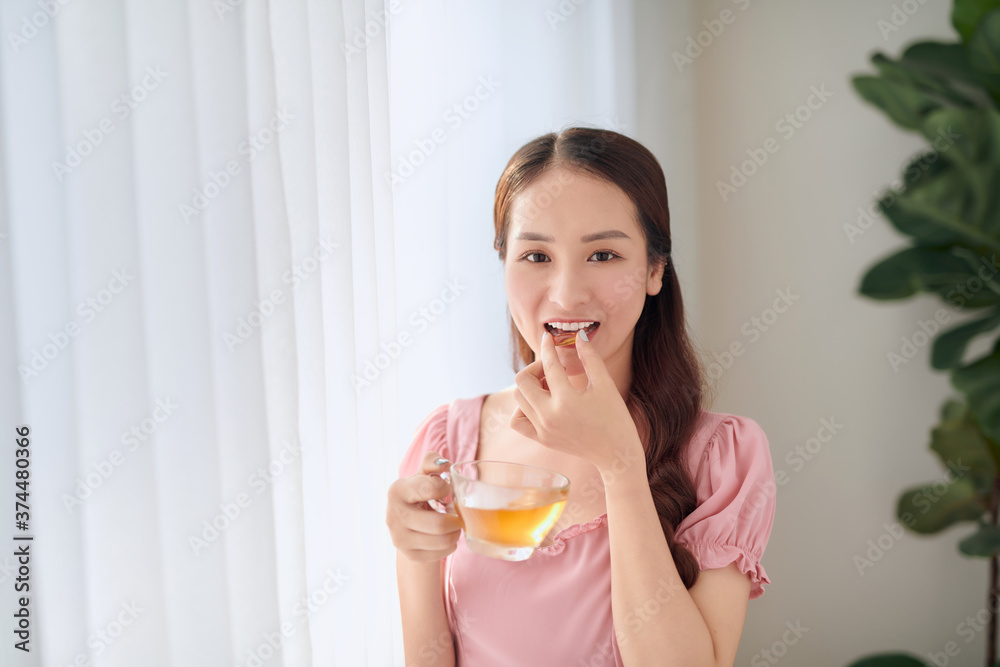 Young beautiful Asian woman eating pill and drinking water