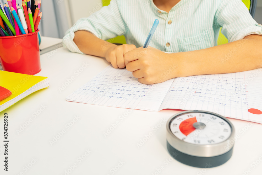 Little boy with lesson timer while doing writing exercise on background