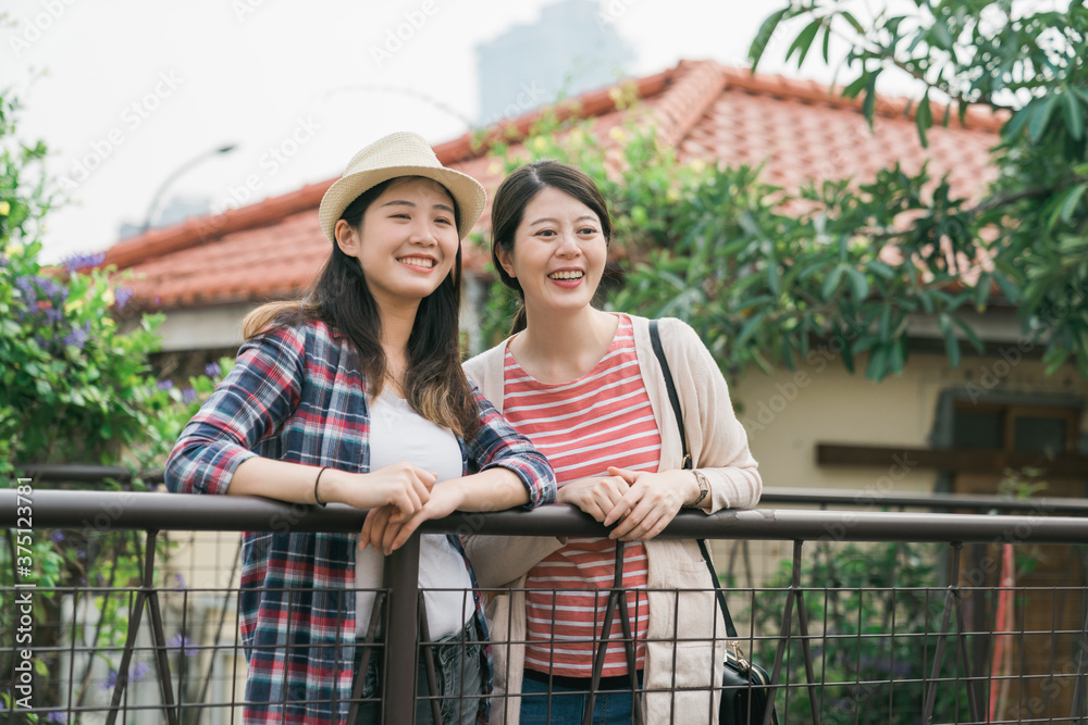 两个穿着春装的亚裔日本美女朋友站在户外，靠在栏杆上