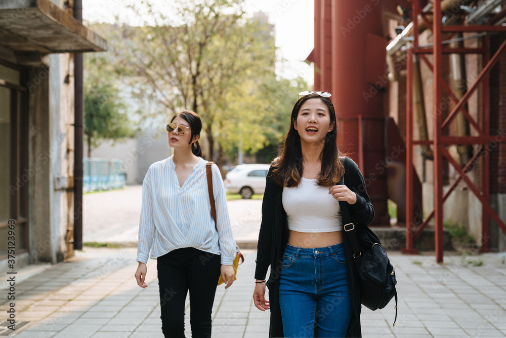 两个戴着墨镜、背着包的快乐女孩在夏天的日落时分走在户外。快乐的asi