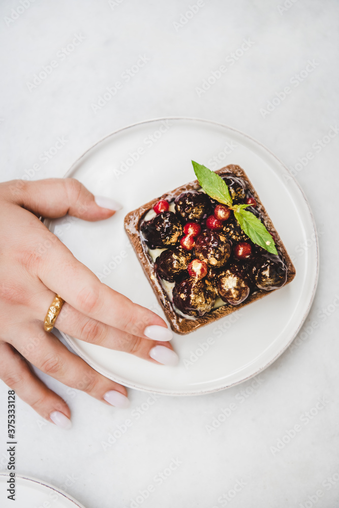 Flat-lay of woman taking cocoa tartalette with fresh seasonal berries from white plate by hand, top 