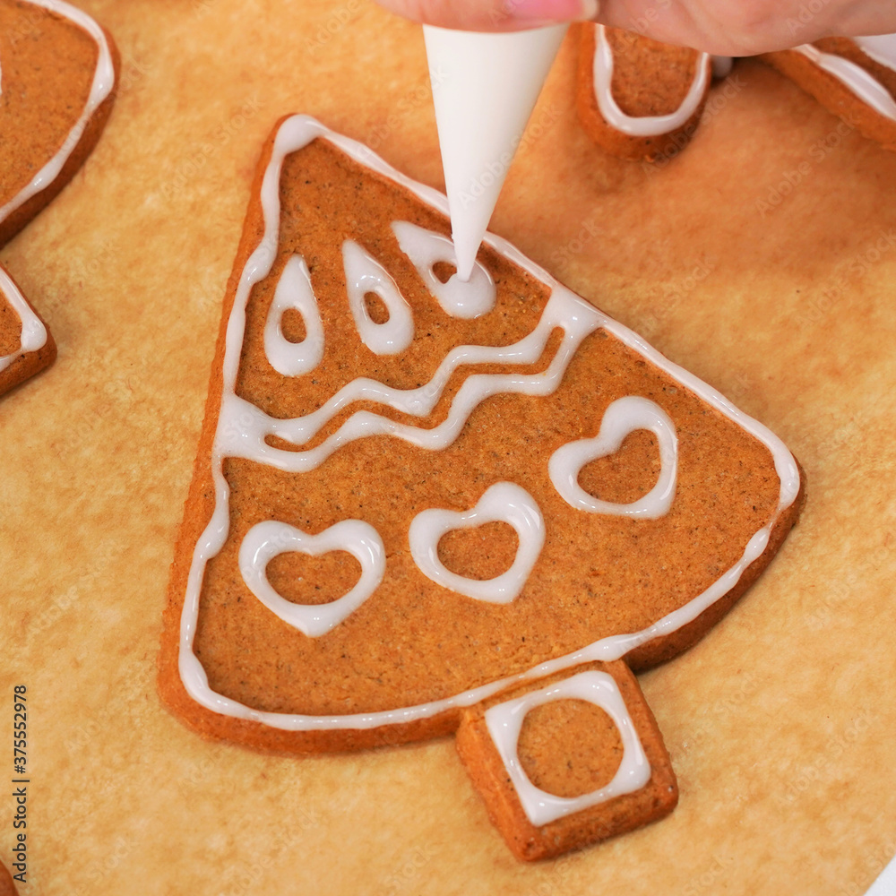 Young woman is decorating Christmas Gingerbread House cookies biscuit at home with frosting topping 