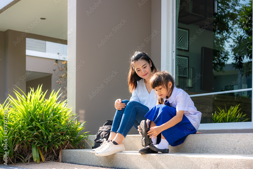 一位亚洲母亲看着她女儿小学生穿着制服在面前穿自己的鞋子