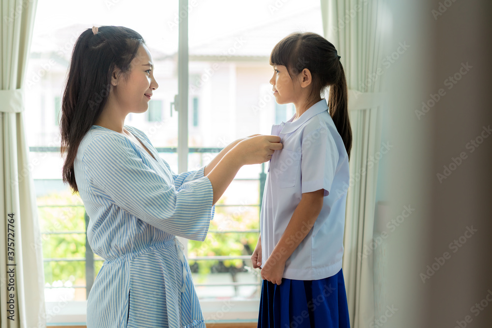 亚洲母亲在h的客厅里为她的小女儿准备小学校服