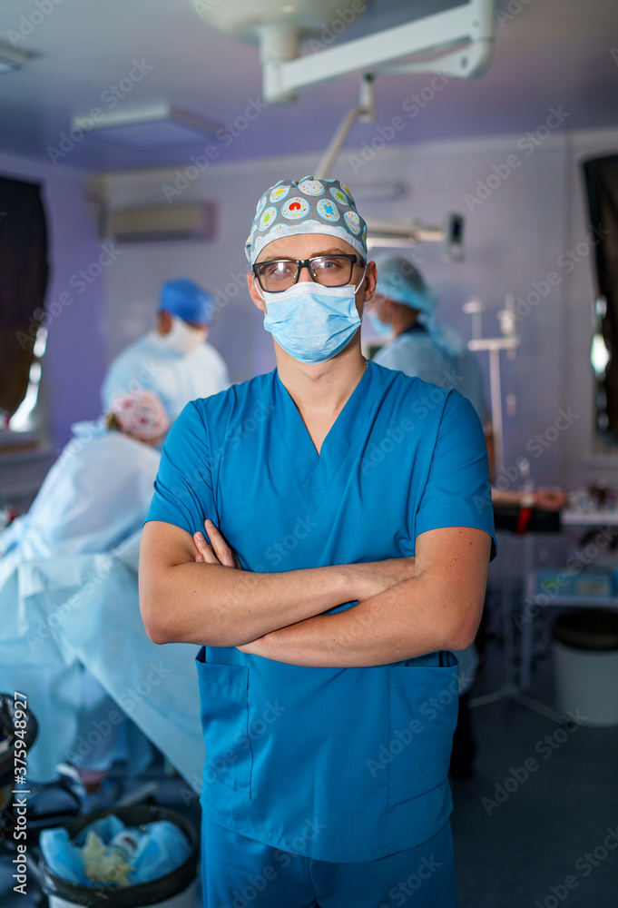 Doctor stands cross hands. Blue scrubs. Robotic medical equipment background. Medical team working. 