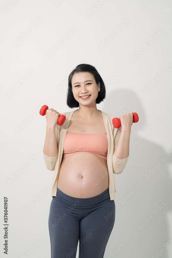 Closeup of pregnant woman doing exercises with dumbbells in the room