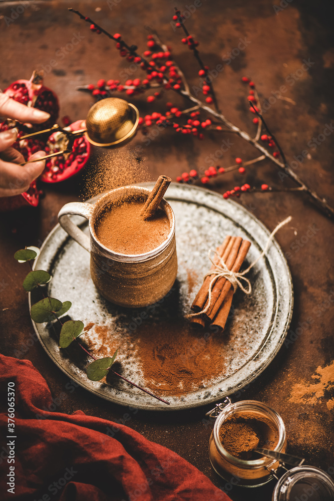 土耳其传统冬季热饮Salep。人手将肉桂粉倒入一杯甜w中