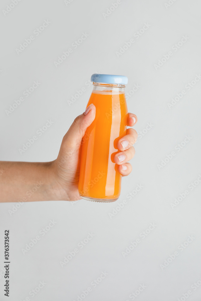 Female hand with bottle of juice on light background