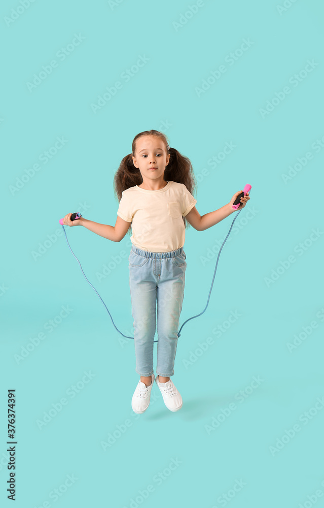 Cute little girl jumping rope against color background